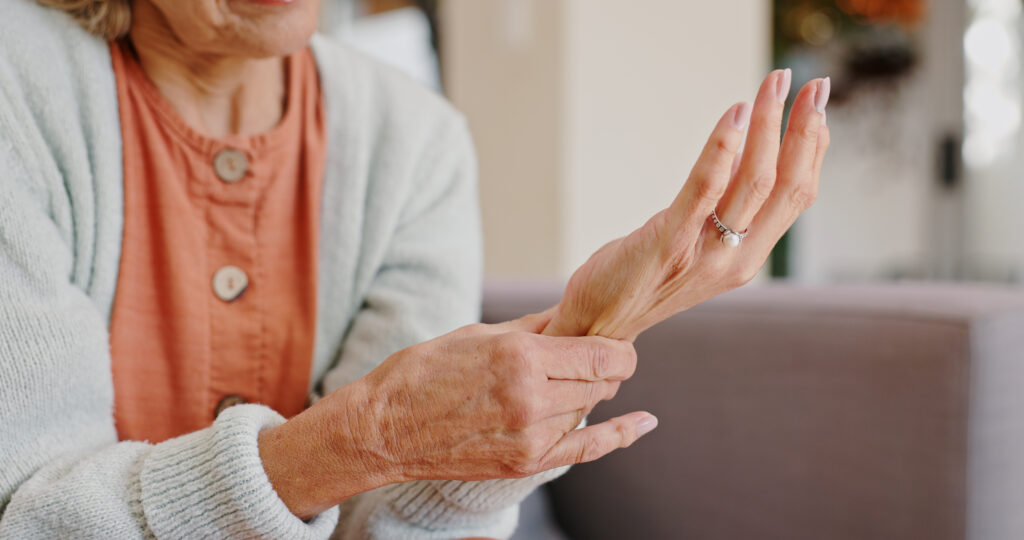 Medical, wrist pain and senior person with arthritis, osteoporosis and fibromyalgia on sofa. Home, lounge and woman with hands massage for discomfort, bruise muscle and carpal tunnel in retirement.