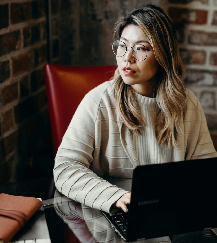 Lady sitting at a table looking out while hands placed on a laptop