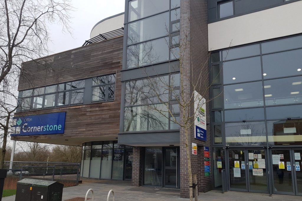 This building is made up mainly of glass windows and doors. The outside is dark grey bricks and blue branded signs.