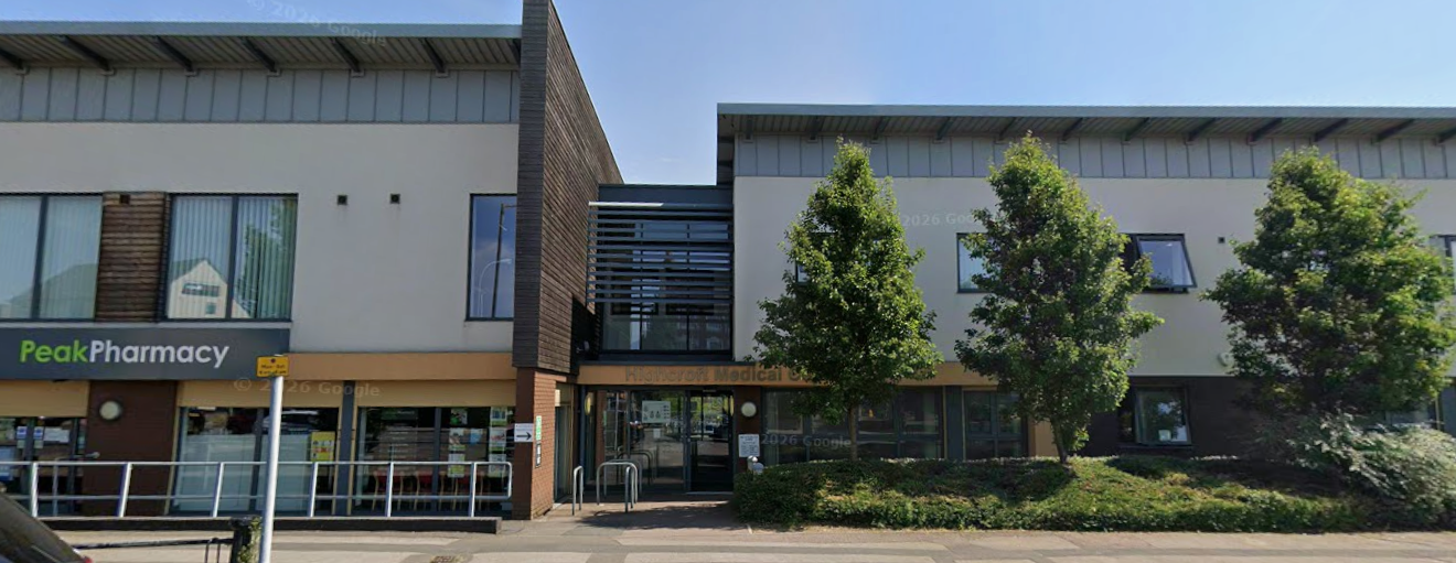 A modern grey building with 3 green trees outside , next to the clinic glass sliding doors is Peak pharmacy you can see 