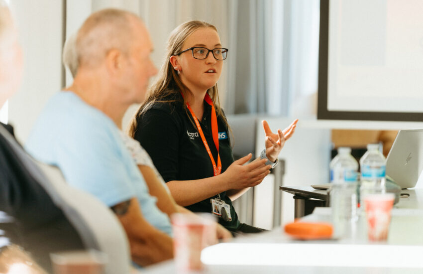 A Cora Health colleague explaining information to event attendees at in a conference room