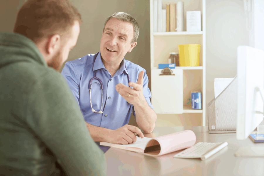 A male consultant smiling and explaining a treatment to a male patient