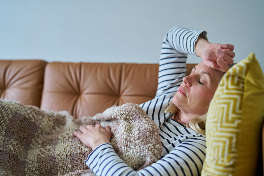 Lady laying on a sofa, eyes closed resting with a blanket and yellow pillow.