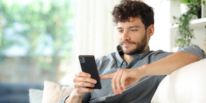 Serious man using smart phone sitting on a couch at home