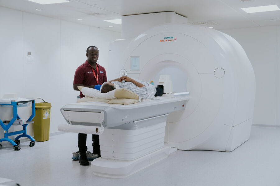 Male clinician supporting patient into a MRI machine.