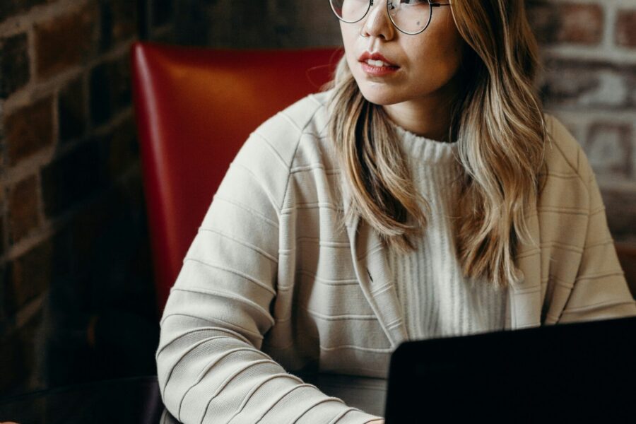 Lady sitting at a table looking out while hands placed on a laptop