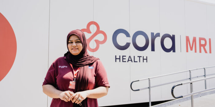 Lady wearing a maroon cora branded t-shirt infront of the cora branded mobile MRI unit
